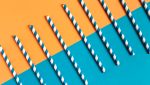 Blue and orange striped biodegradable paper straws on a matching blue and orange background, promoting eco-friendly choices.