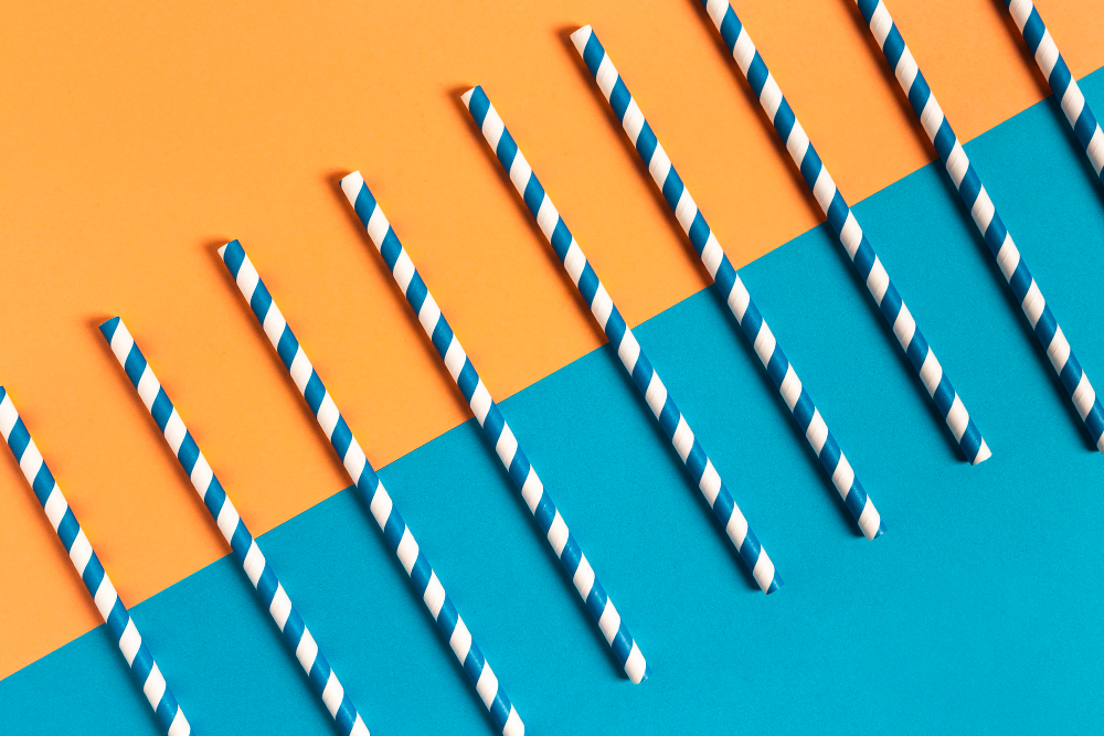 Blue and orange striped biodegradable paper straws on a matching blue and orange background, promoting eco-friendly choices.