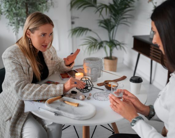 Two women at a candlelit table, engaged in a thoughtful discussion over tea about accurate and compassionate psychic insights.