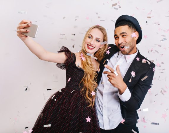 A man and woman smiling for a selfie as confetti falls around them, representing the joy of affordable photo booth rentals in Texas.