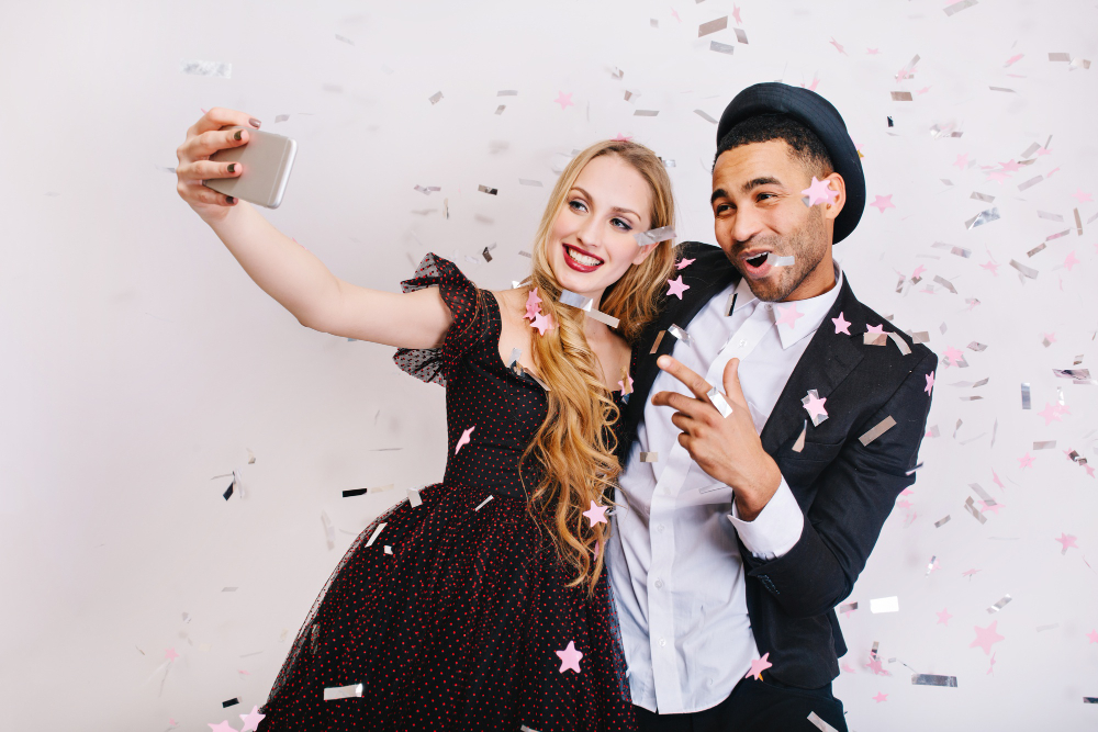 A man and woman smiling for a selfie as confetti falls around them, representing the joy of affordable photo booth rentals in Texas.